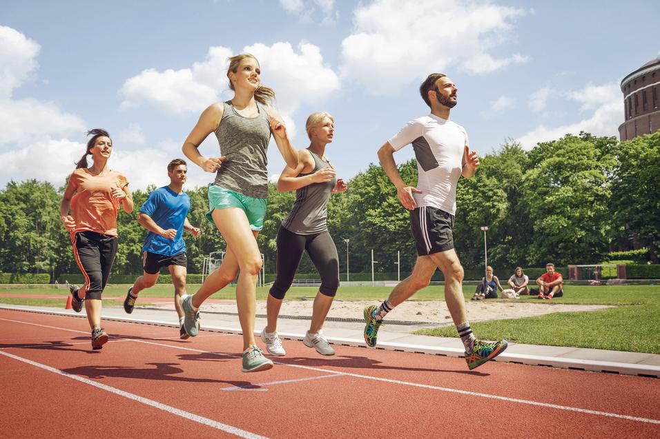 Fünf Erwachsene laufen gemeinsam auf einer Laufbahn im Stadion bei Sonnenschein.