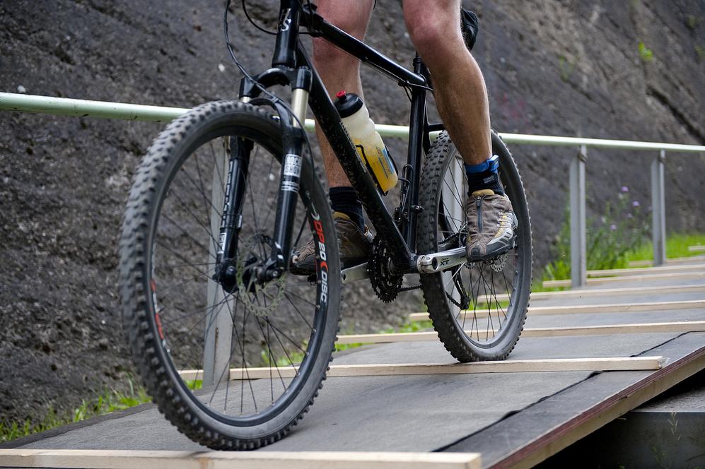 Nahaufnahme eines Mountainbikes mit Fahrer auf einer Holzrampe mit grünem Hintergrund.